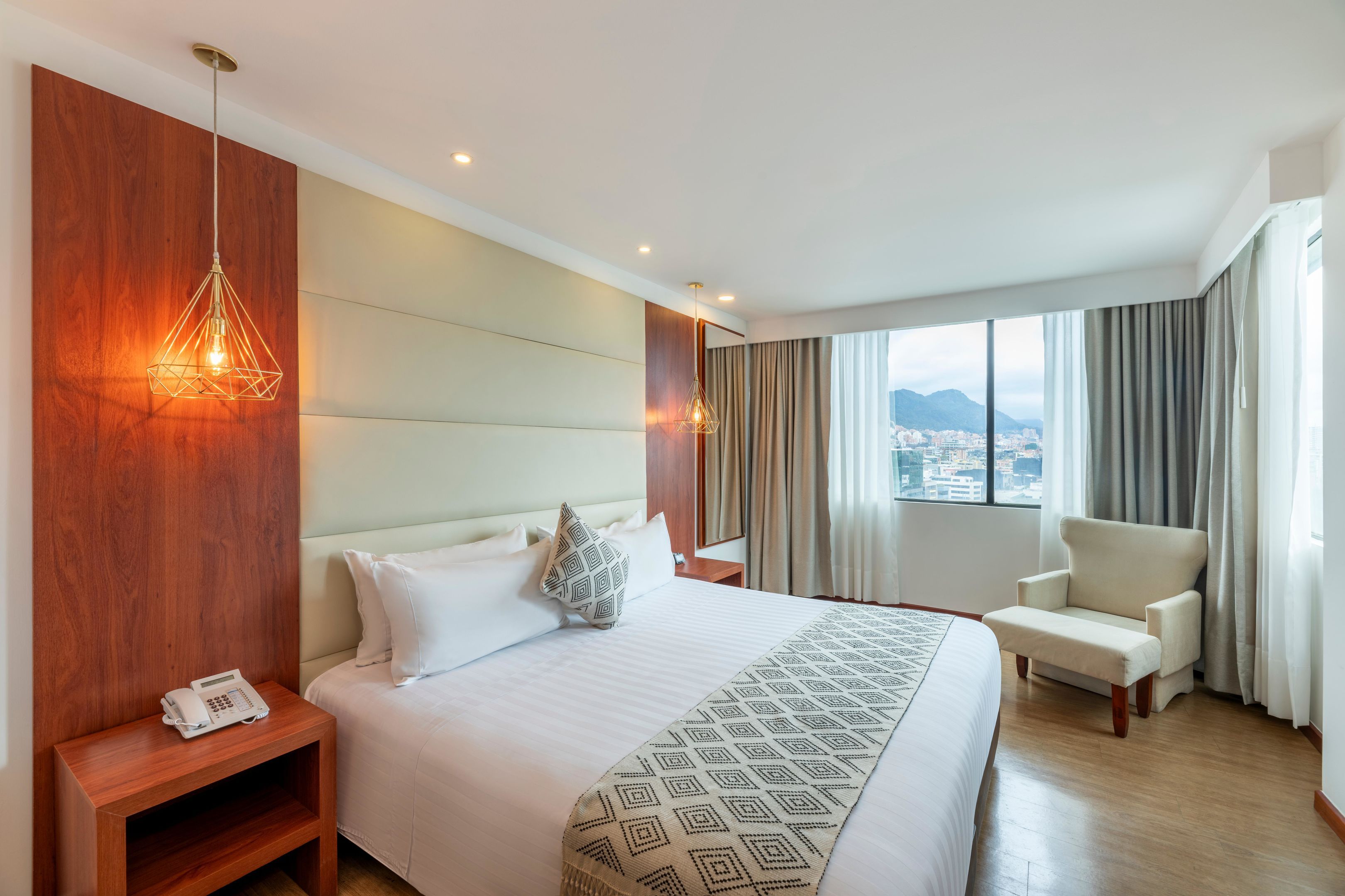 Une chambre d’hôtel avec un grand lit, des tables de chevet, une chaise et une vue sur la ville par la fenêtre.