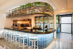 Una zona de bar con una barra curva, diversas opciones de asiento y una variedad de botellas y vasos en estanterías.