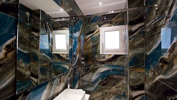 A bathroom with a white sink, a glass shower enclosure, and marble-patterned walls.