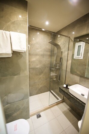 A modern bathroom with a glass-enclosed shower, a white sink, and a marble-tiled floor.