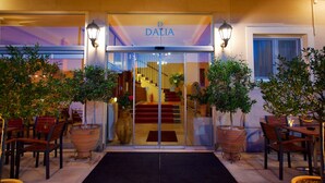 La entrada de un hotel con puerta de cristal, plantas en macetas y una escalera que conduce al interior.