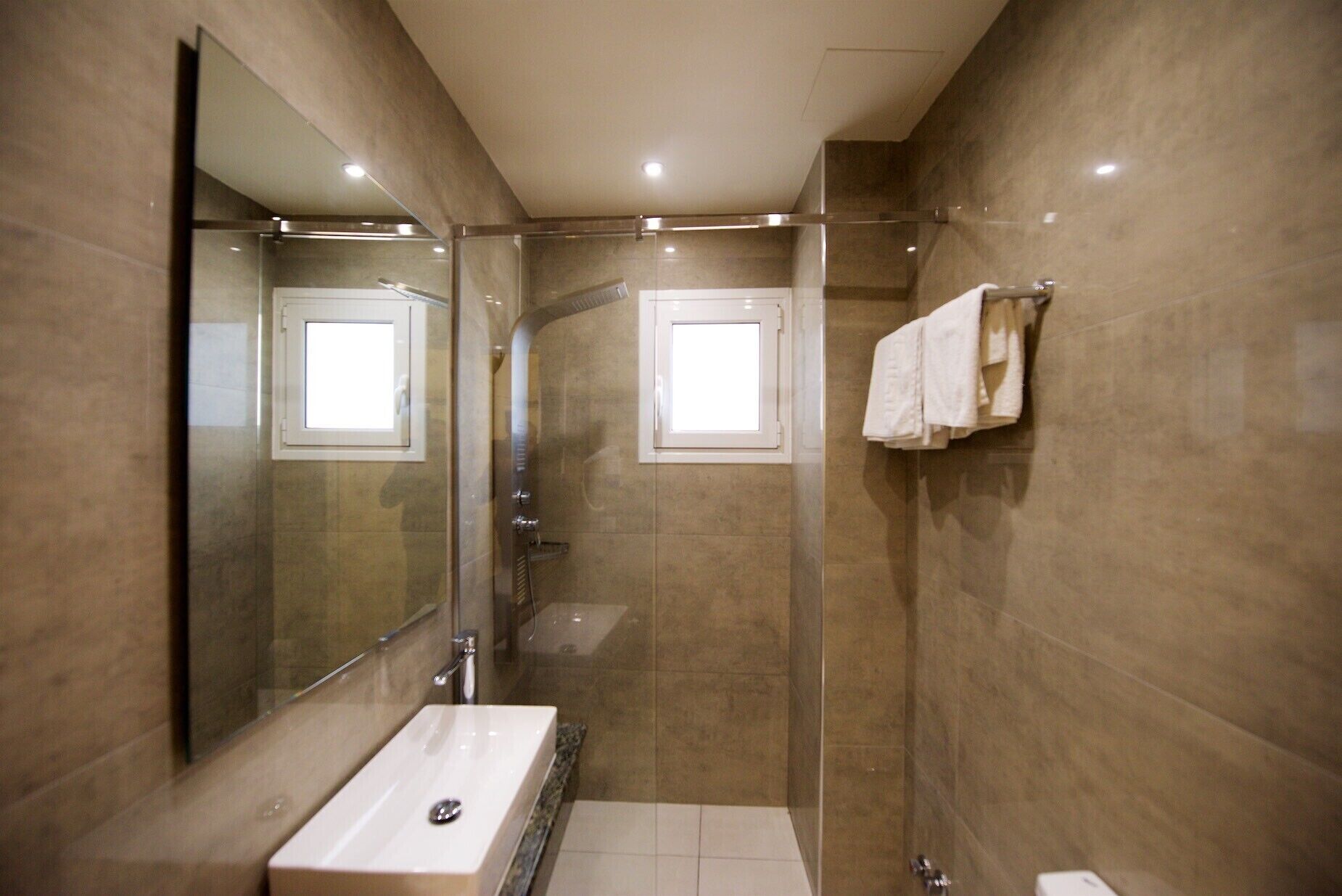 Un baño moderno con un espejo grande, un lavabo, una ducha y un perchero para toallas.