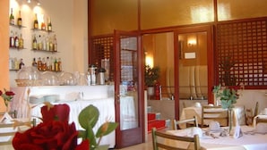 Un restaurante con mesas dispuestas para comer, una zona de bar con botellas y una partición decorativa de madera.