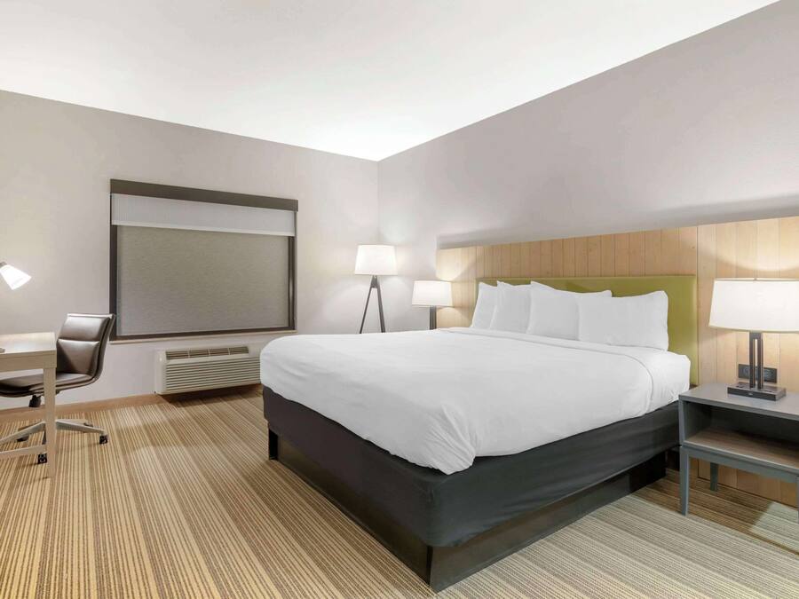 Une chambre d’hôtel avec un grand lit, des tables de chevet avec des lampes, un bureau avec une chaise et une grande fenêtre.