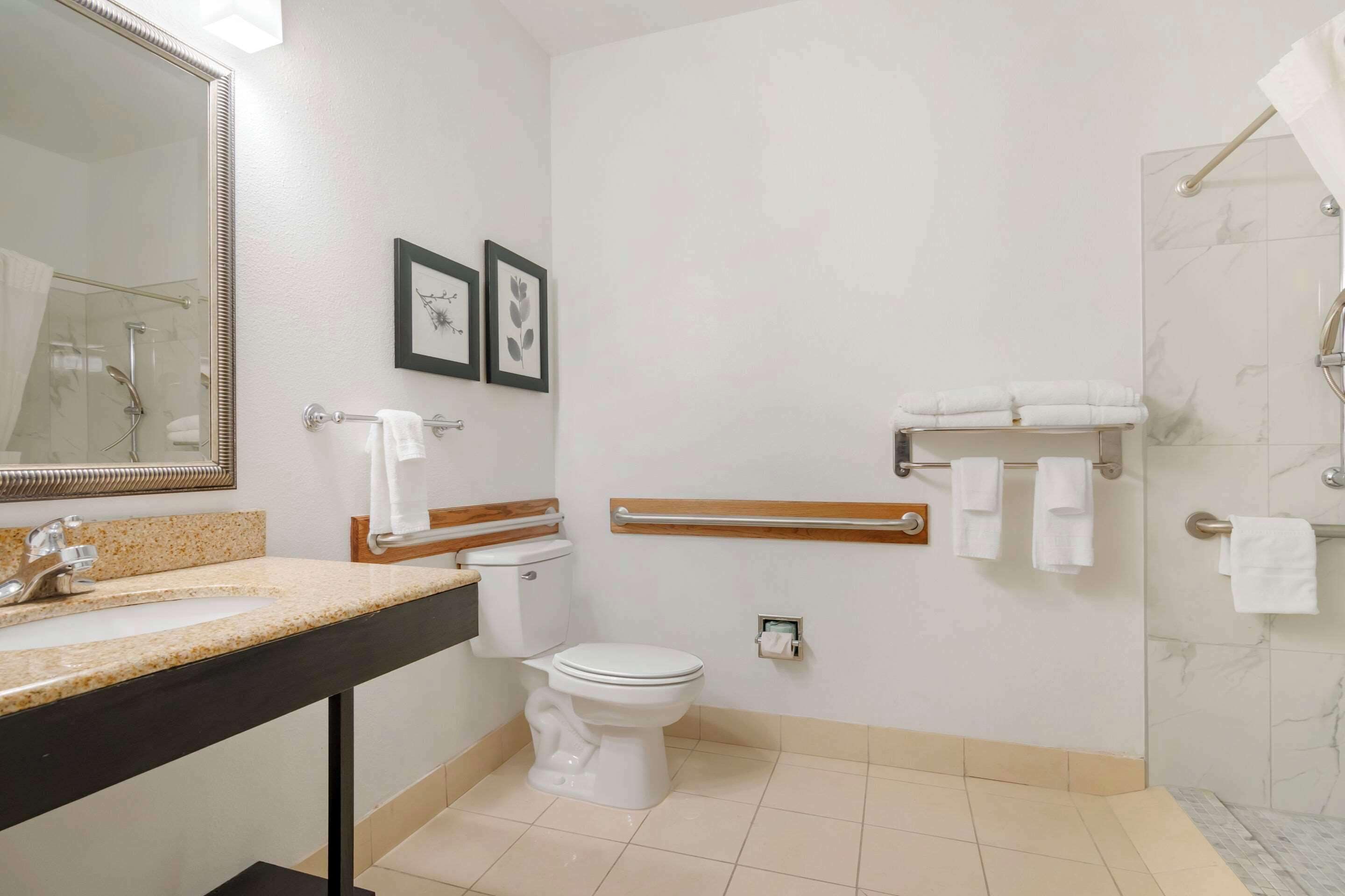 Un baño moderno con lavamanos, inodoro y ducha. Hay fotografías enmarcadas en la pared y un perchero para toallas.