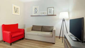 Una sala de estar con un sillón rojo, un sofá beige, un televisor sobre un mueble bajo y una lámpara de pie.