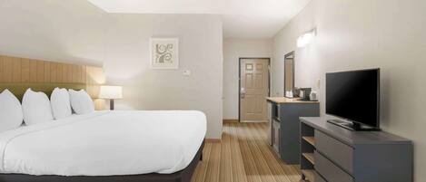Una camera d'albergo con un letto grande, una TV, una scrivania e un bagno visibile tramite una porta aperta.
