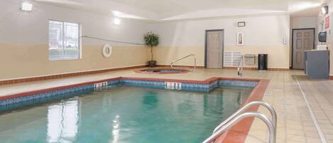 An indoor swimming pool with a tiled edge, a handrail, and a potted plant.