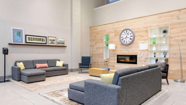 A modern living room with grey sofas, a coffee table, and a fireplace. There are framed pictures on the wall and a floor lamp. - Country Inn & Suites by Radisson, Columbia, MO (Columbia)