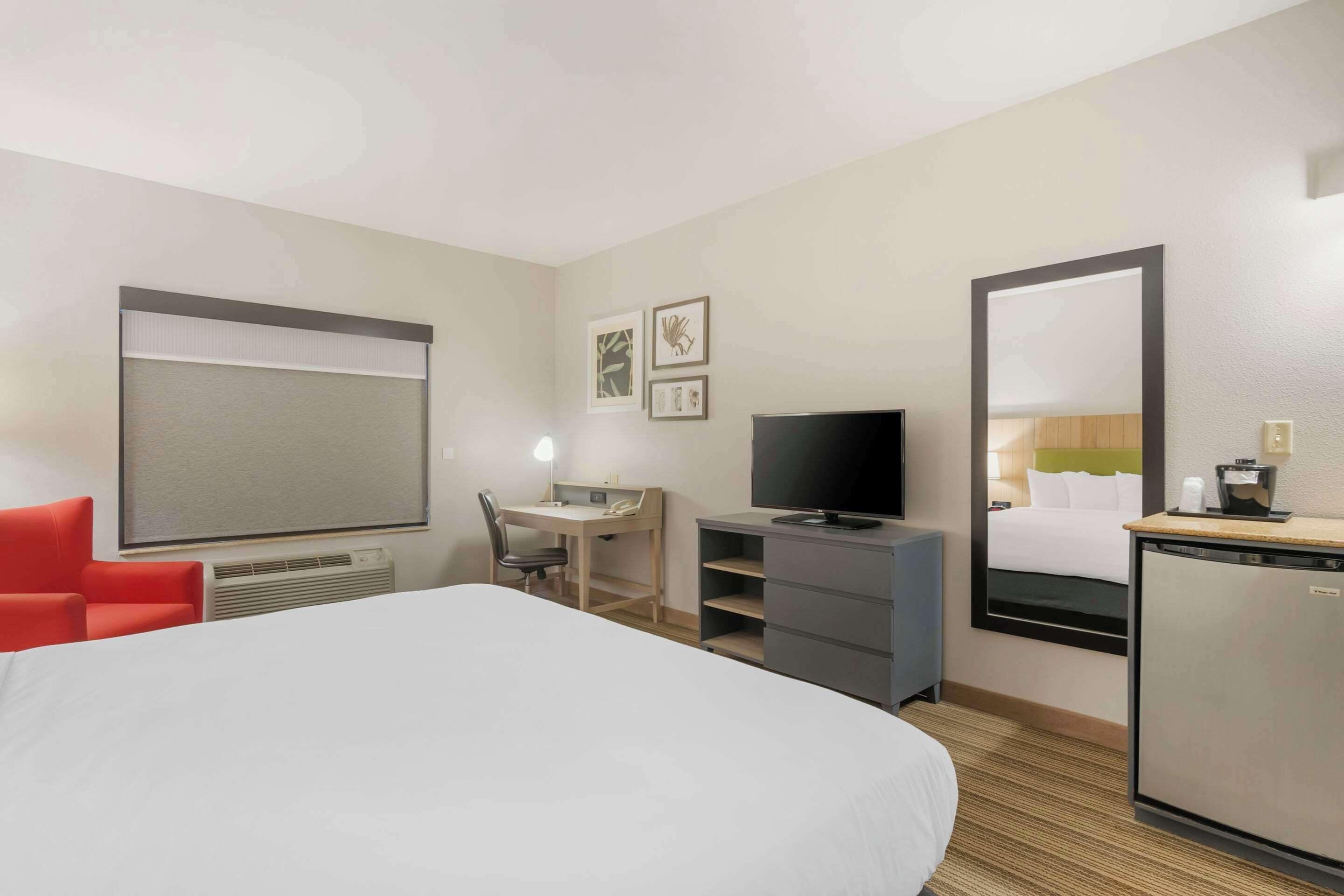 Une chambre d’hôtel avec un grand lit, un bureau avec une chaise, une télévision, un petit réfrigérateur et un miroir.