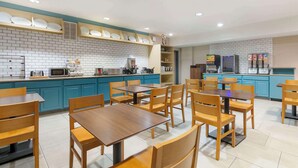 A modern restaurant with blue cabinets, wooden tables and chairs, and a kitchen area with appliances. - Country Inn & Suites by Radisson, Columbia, MO (Columbia)