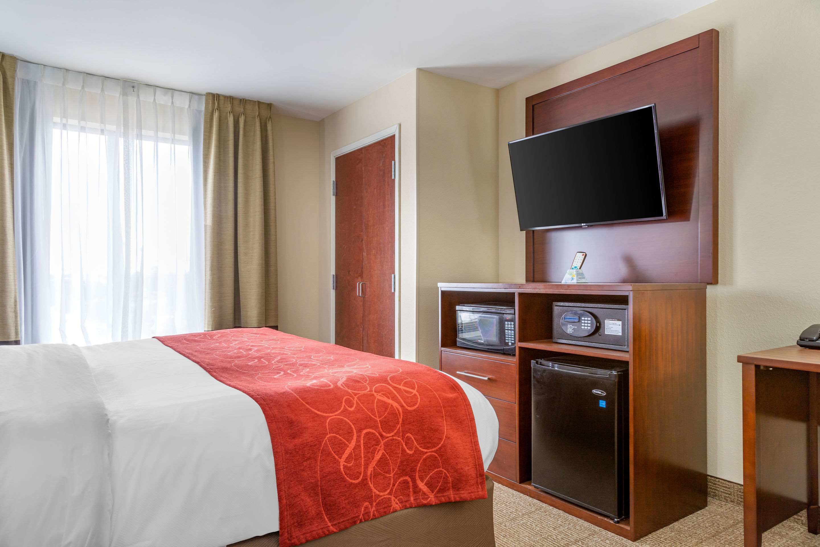 Quarto de hotel com cama, televisão na parede, micro-ondas e frigorífico.
