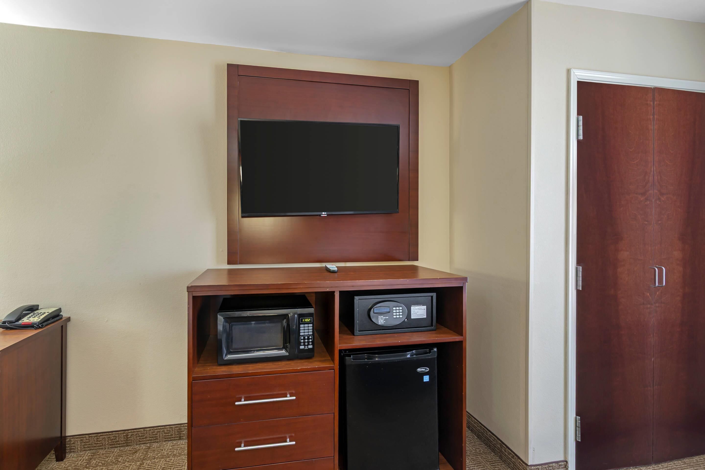 Een compacte kamer met een flatscreen televisie bevestigd aan een houten kast, een magnetron en een minibar.