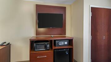 Een compacte kamer met een flatscreen televisie bevestigd aan een houten kast, een magnetron en een minibar.