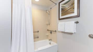 A modern bathroom with a bathtub, shower, and handrails.