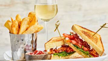 En halv sandwich, et glas hvidvin og en metal kop med pommes frites.