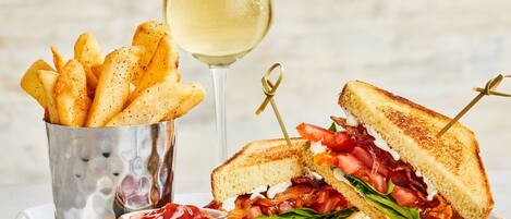 A sandwich cut in half, a glass of white wine, and a metal cup of fries.