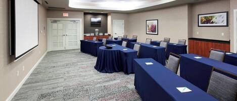 A conference room with tables covered in blue cloths, a projector screen, and a carpeted floor.