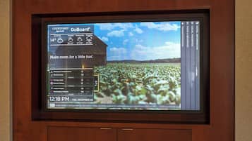 Um visor digital exibindo previsão do tempo, placar esportivo e vista de um campo.