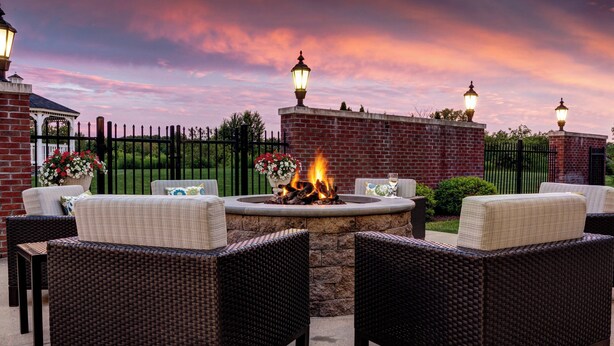 An outdoor seating area with wicker furniture, a fire pit, and decorative lamps. - Courtyard by Marriott Hadley Amherst (Hadley)