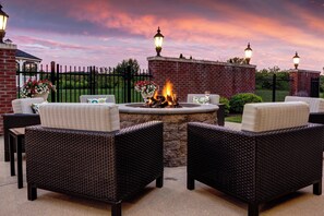 An outdoor seating area with wicker furniture, a fire pit, and decorative lamps. - Courtyard by Marriott Hadley Amherst (Hadley)