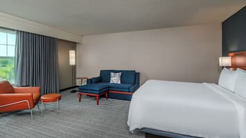 Una habitación de hotel con una cama, un sofá, una silla, una mesita y una lámpara.