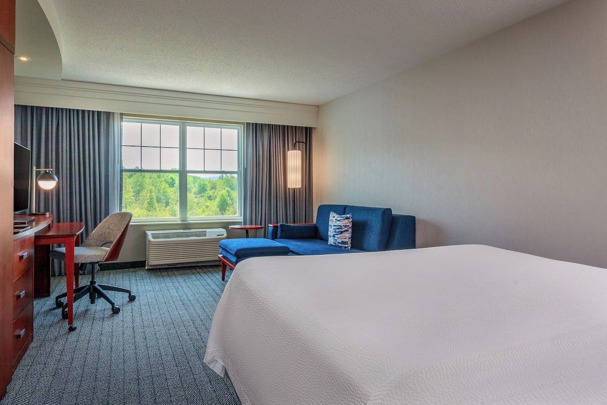A hotel room with a large bed, a desk with a chair, a sofa, and a large window with curtains.