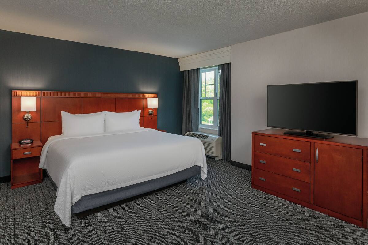 A hotel room with a large bed, a TV on a wooden cabinet, and a window with curtains.