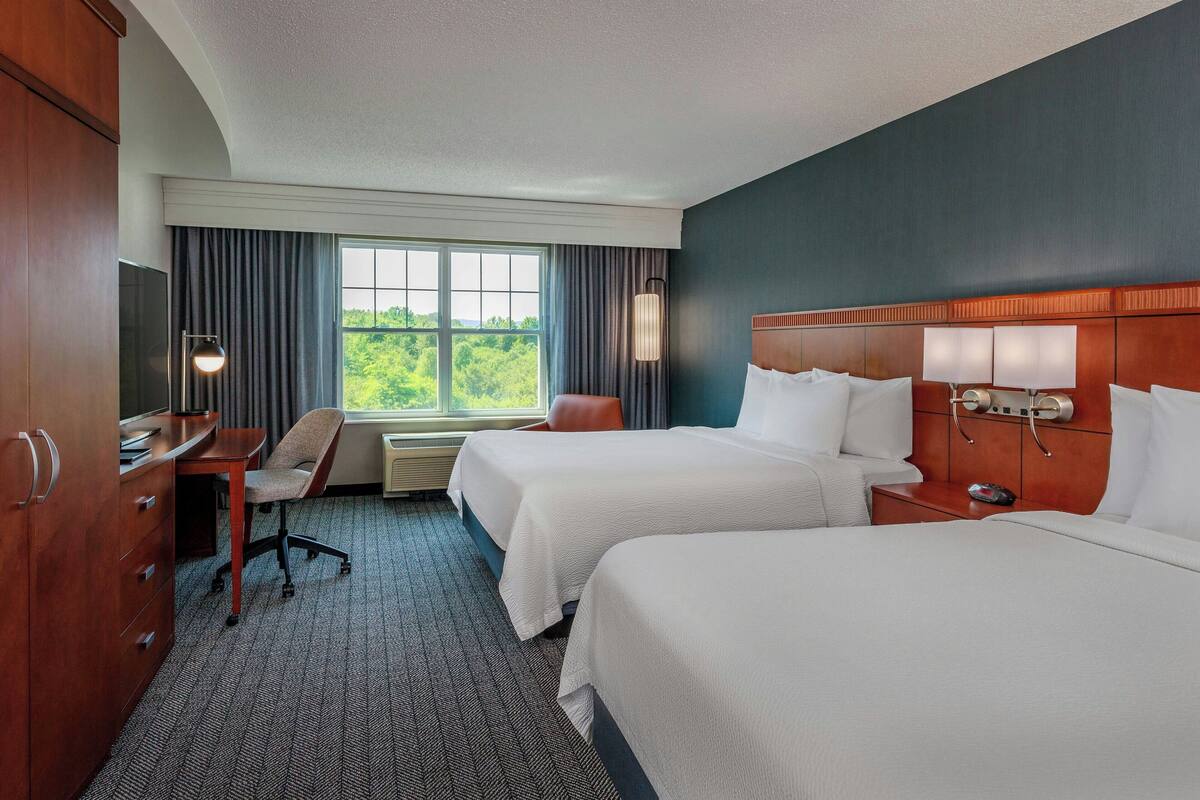 A hotel room with two beds, a desk, a chair, a TV, and a window with curtains.