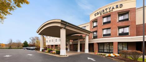 A Courtyard by Marriott hotel entrance with a covered walkway, brick facade, and a parking lot.