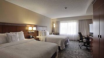 A hotel room with two beds, a desk, a chair, a TV, and a window with curtains.