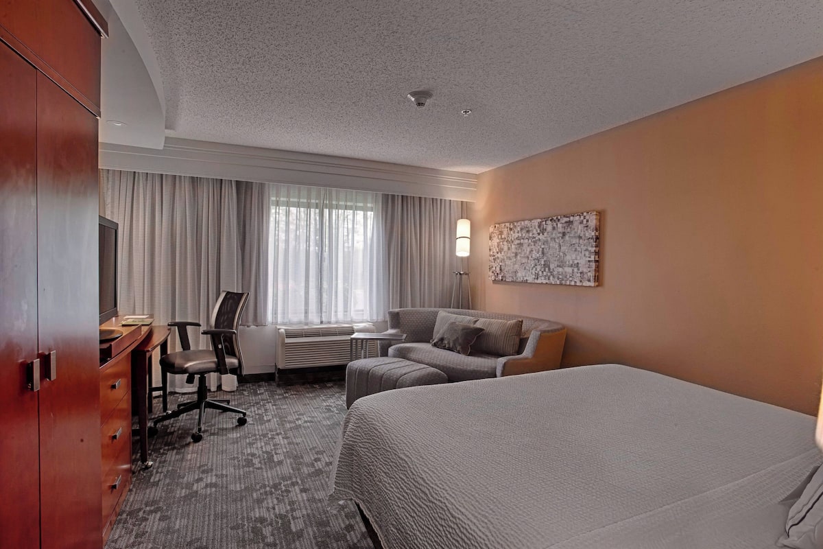 Une chambre d’hôtel avec un grand lit, un bureau avec une chaise, un canapé et une œuvre d’art accrochée au mur.
