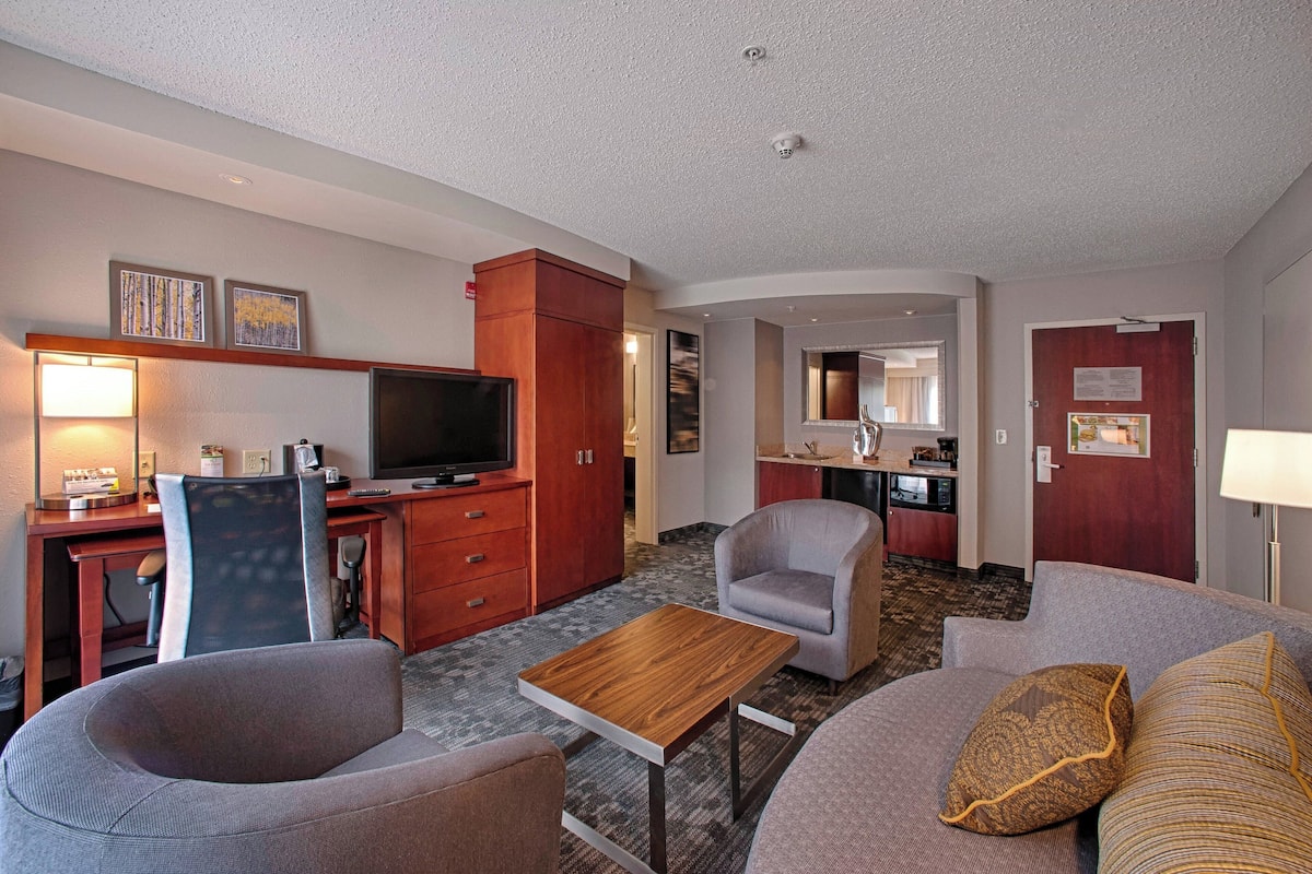 Une chambre d’hôtel comprenant un coin salon, une kitchenette, une télévision et un bureau.