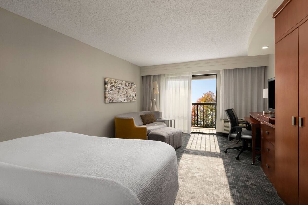 Une chambre d’hôtel avec un grand lit, un bureau, une chaise, un canapé et un balcon avec vue.