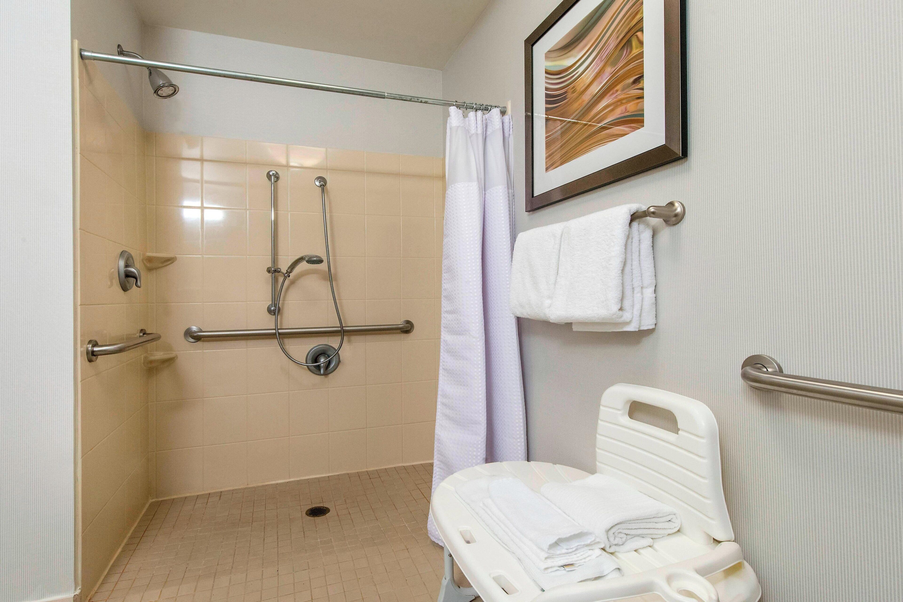 Une douche équipée d’une barre d’appui, d’un banc accessible aux personnes en fauteuil roulant et d’une main courante.