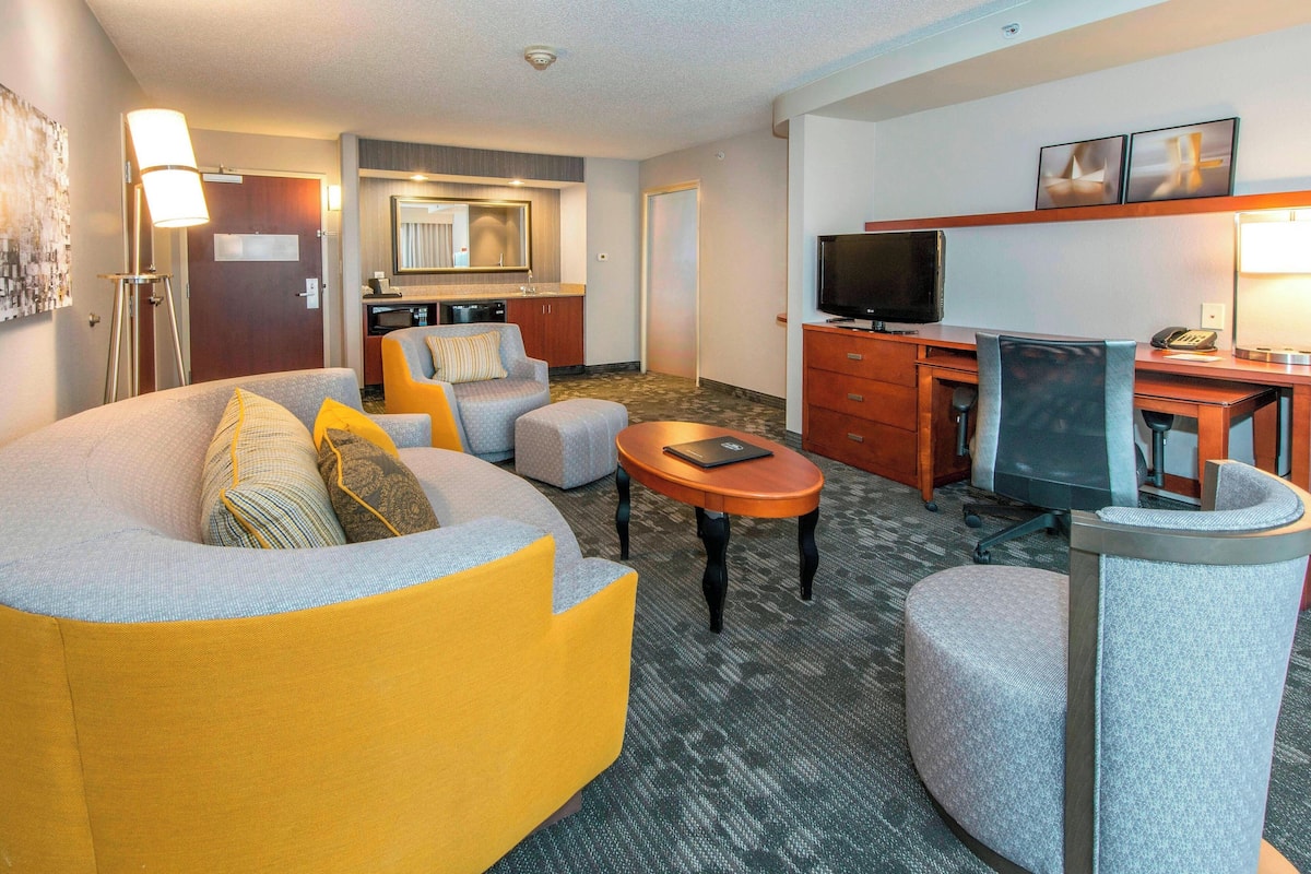 Une chambre d’hôtel équipée d’un canapé, d’un fauteuil, d’un bureau, d’une télévision et d’une petite kitchenette.
