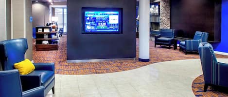 A lobby with blue seating, a large digital display, and a stone accent wall.
