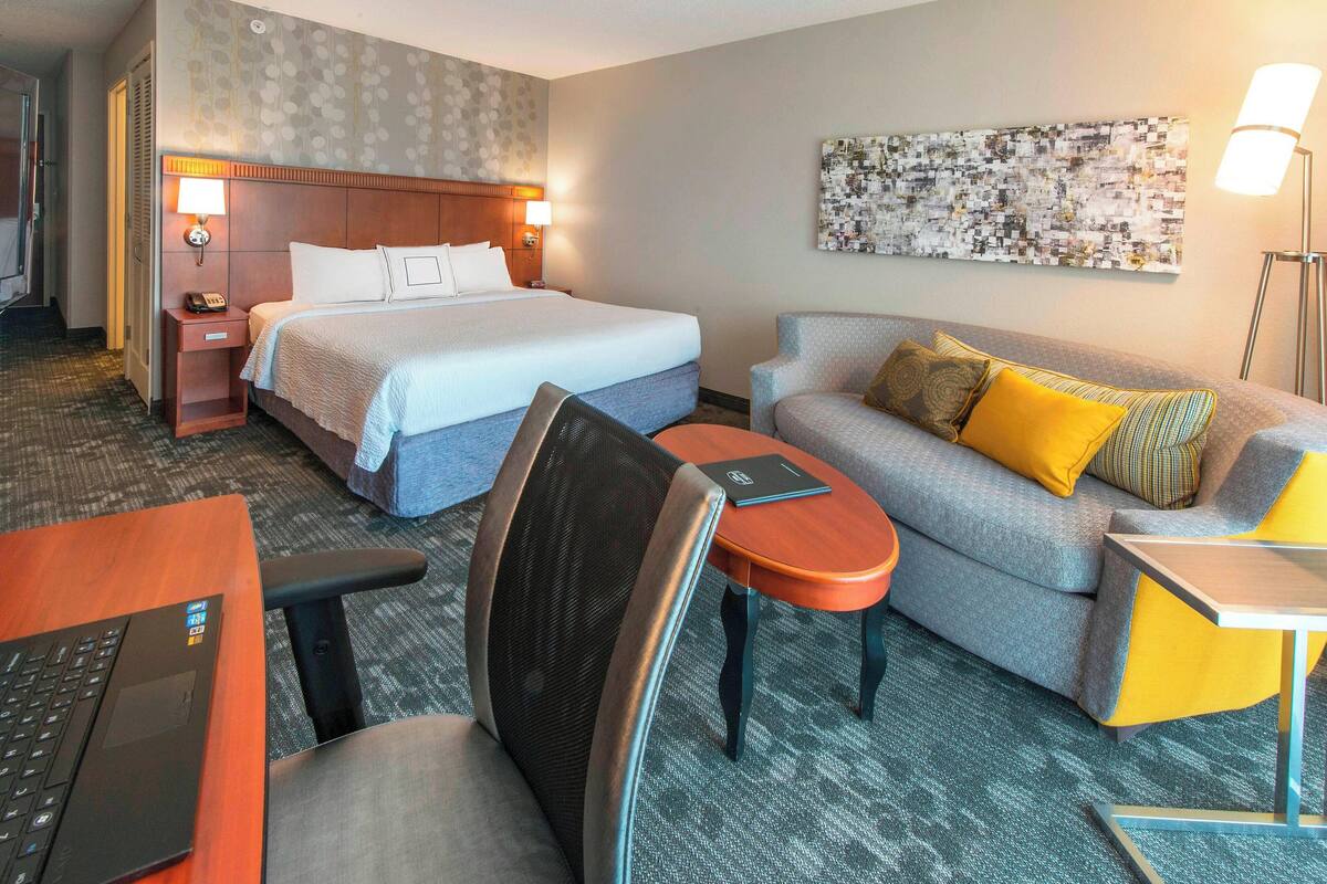 Ein Hotelzimmer mit Bett, einer Couch, einem Schreibtisch und einem Laptop.