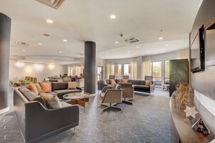 Um hall amplo com assentos modernos, balcão de recepção e grandes janelas que permitem entrada de luz natural.