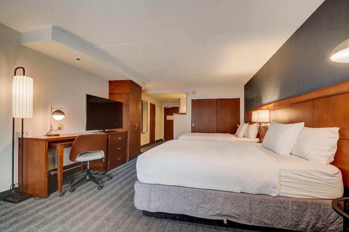 A hotel room with a large bed, a desk with a chair, a television, and a lamp.