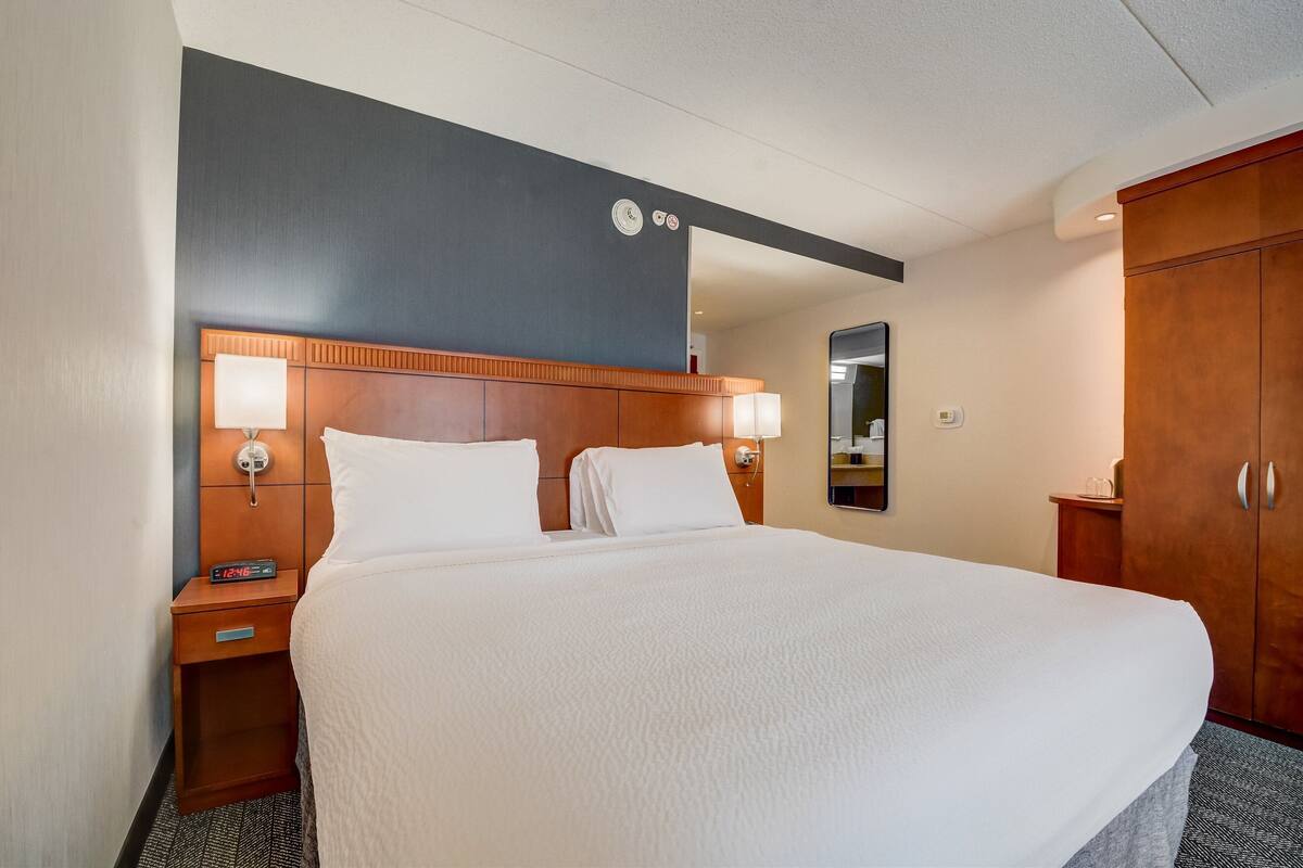 A hotel room with a large bed, wooden headboard, bedside lamps, a nightstand, and a wardrobe.