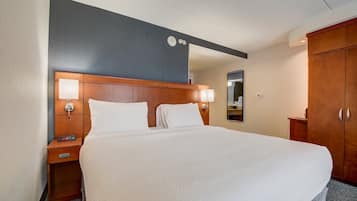 A hotel room with a large bed, wooden headboard, bedside lamps, a nightstand, and a wardrobe.
