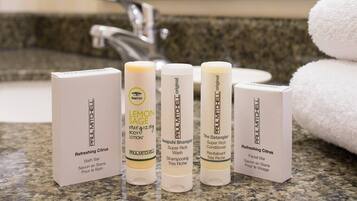 A bathroom counter with four Paul Mitchell products: Refreshing Citrus Bath Bar, Lemon Sage Energizing Body Lotion, Awapuhi Shampoo, and The Detangler Super Rich Conditioner.