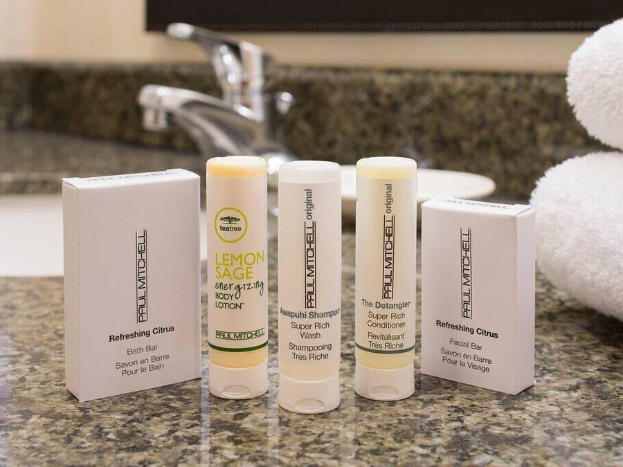 A bathroom counter with four Paul Mitchell products: Refreshing Citrus Bath Bar, Lemon Sage Energizing Body Lotion, Awapuhi Shampoo, and The Detangler Super Rich Conditioner.