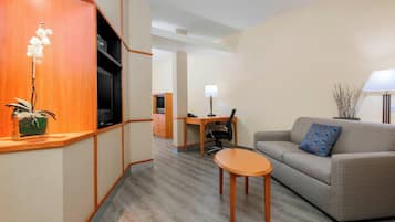 Una habitación de hotel moderna con un mostrador de recepción de madera, un sofá con un cojín estampado, una mesita y una lámpara.