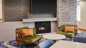 A modern living room with a fireplace, two green sofas, a flat-screen TV, and a stone accent wall. - Fairfield Inn & Suites by Marriott Burlington (Burlington)