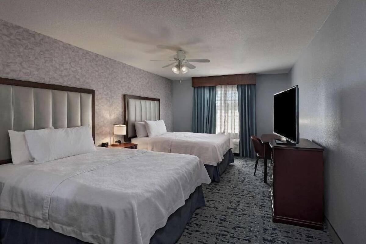 A hotel room with two beds, a ceiling fan, a flat-screen TV, and a desk.