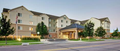 A multi-story hotel with a central entrance, a flagpole, and a landscaped front yard.