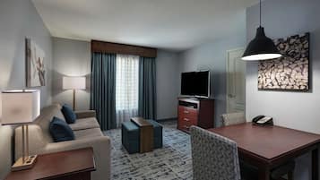 Ein Hotelzimmer mit einer Couch, einem Couchtisch, einem Fernseher, einem Schreibtisch, einem Stuhl, einer Lampe und einem Telefon.