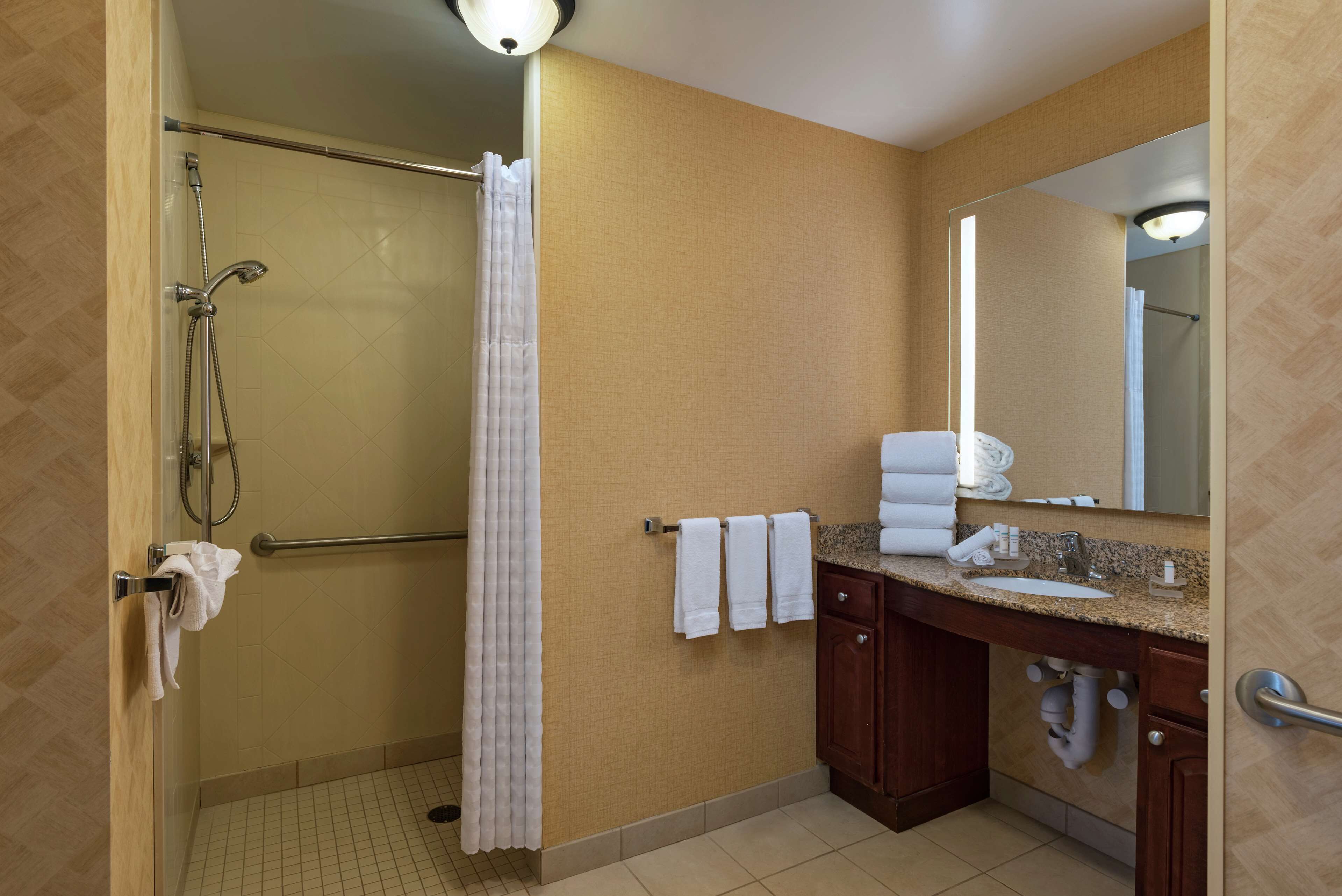 A hotel bathroom with a shower, a sink, a mirror, and towels.